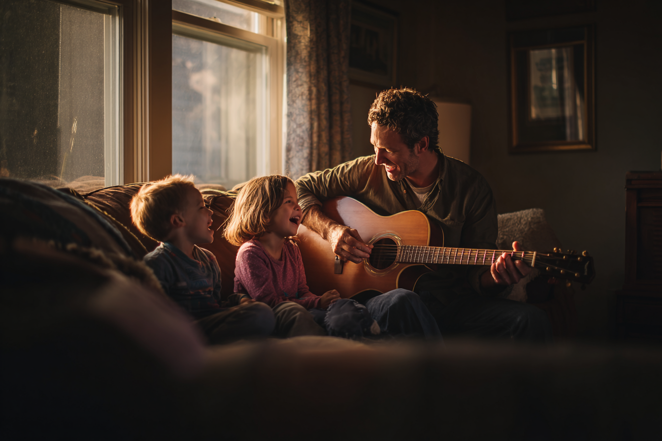 Father playing guitar for his two children on a couch.